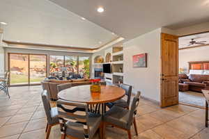 Dining room featuring a tile fireplace, built in shelves, a tray ceiling, and ceiling fan