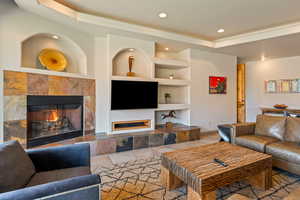 Tiled living room with a raised ceiling, a tile fireplace, built in features, and recessed lighting