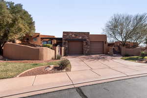 Pueblo revival-style home with a gate, stone siding, driveway, stucco siding, and an attached garage