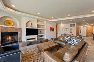 Living room featuring a tiled fireplace, built in features, a tray ceiling, recessed lighting, and light tile patterned flooring