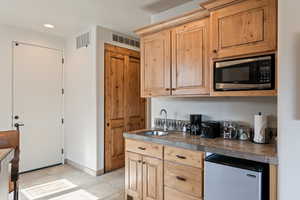 Kitchen featuring light brown cabinetry, fridge, stainless steel microwave, recessed lighting, and tile counters