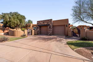 Pueblo-style home with a gate, stucco siding, stone siding, and driveway