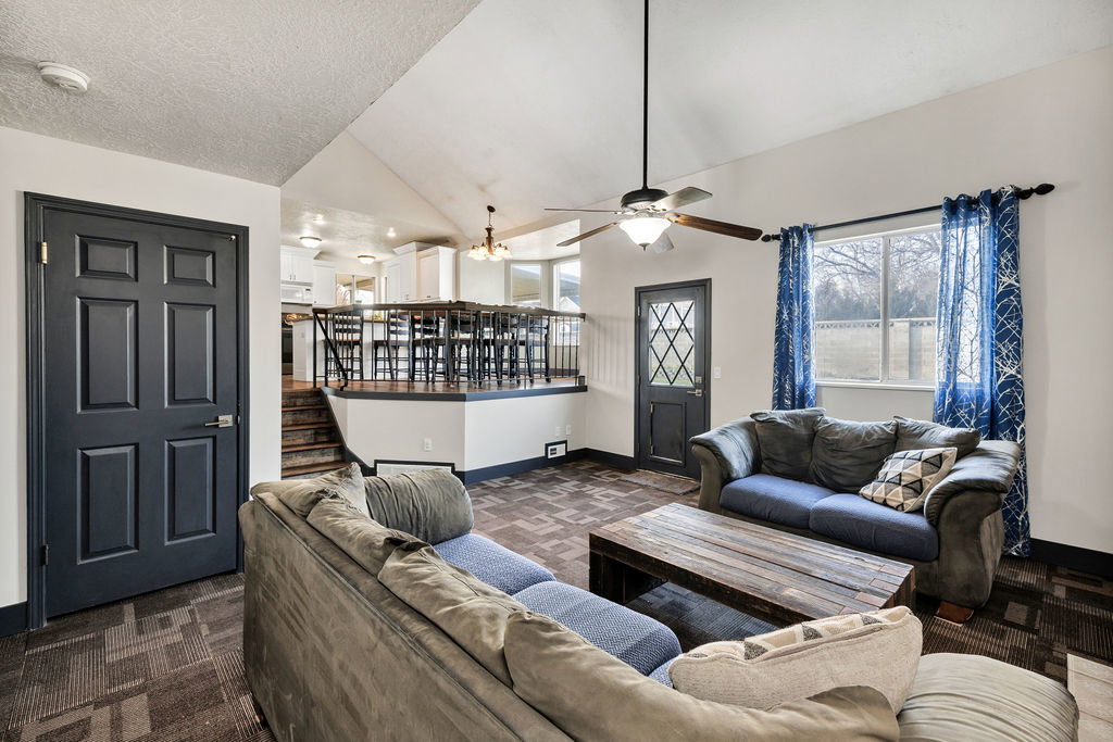 Carpeted living room featuring lofted ceiling, a ceiling fan, and a textured ceiling
