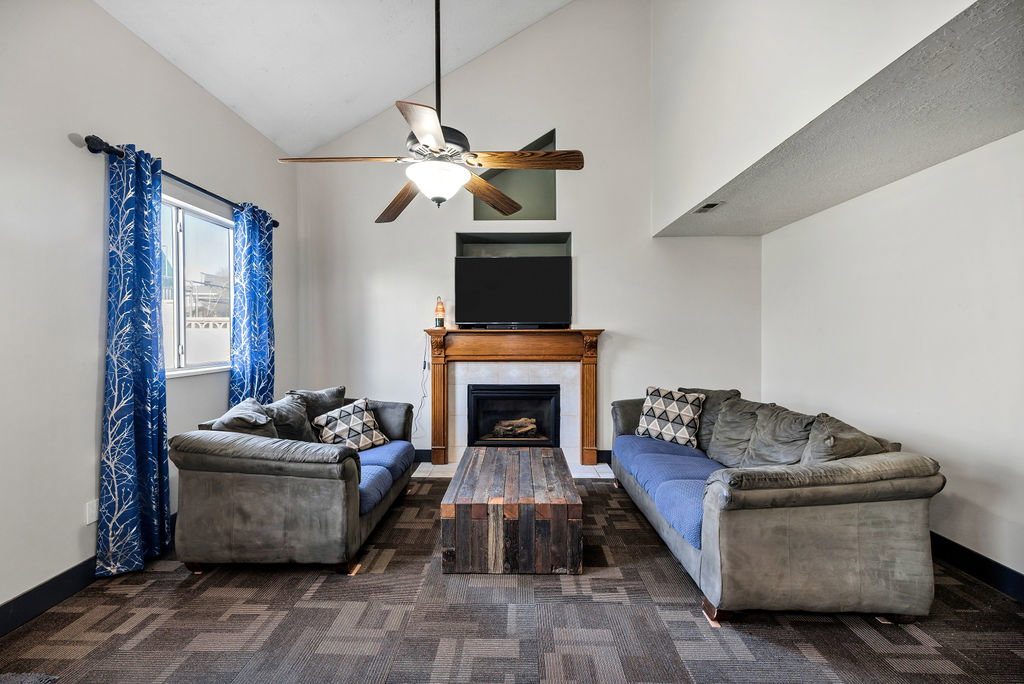 Living area with dark colored carpet, a tiled fireplace, high vaulted ceiling, and a ceiling fan