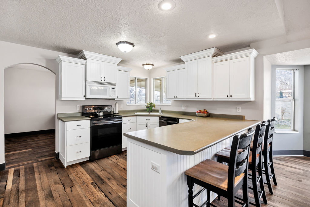 Kitchen featuring electric range, a kitchen bar, white microwave, dark wood-type flooring, and white cabinetry