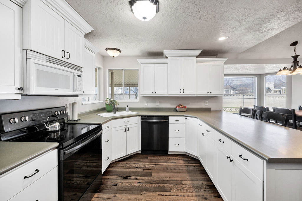 Kitchen with black appliances, white cabinetry, a peninsula, a textured ceiling, and light countertops