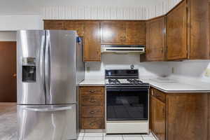 Kitchen featuring stainless steel fridge, black range oven, light countertops, and under cabinet range hood