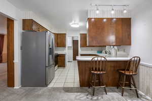 Main level kitchen featuring stainless steel fridge, light countertops, a peninsula, light carpet, and wallpapered walls