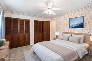 Carpeted bedroom featuring two closets, ceiling fan, and wallpapered walls