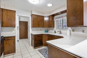 Kitchen featuring light tile patterned floors, black range, wallpapered walls, and brown cabinets