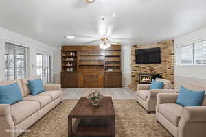 Living room featuring wainscoting, plenty of natural light, a fireplace, ceiling fan, and wood finished floors