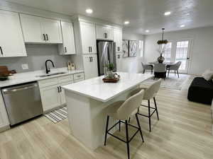 Kitchen with light wood-style floors, white cabinetry, stainless steel appliances, recessed lighting, and a textured ceiling