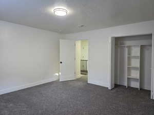 Unfurnished bedroom featuring dark carpet, a textured ceiling, and a closet