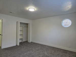 Unfurnished bedroom featuring a textured ceiling, a closet, and dark colored carpet