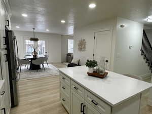 Kitchen with a textured ceiling, hanging light fixtures, a kitchen island, light wood-style flooring, and freestanding refrigerator