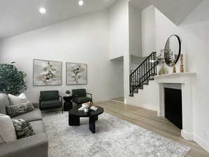 Living area featuring high vaulted ceiling, a fireplace, stairs, and light wood finished floors