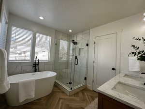 Bathroom featuring a stall shower, a freestanding bath, double vanity, parquet flooring, and recessed lighting