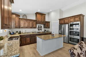 Kitchen featuring dark brown cabinetry, stainless steel appliances, light wood-style floors, dark stone countertops, and high vaulted ceiling
