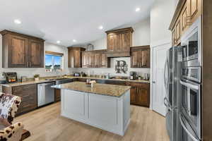 Kitchen with light stone countertops, vaulted ceiling, light wood-style flooring, appliances with stainless steel finishes, and dark brown cabinets