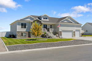 Craftsman-style house featuring stone siding, a porch, a front yard, driveway, and roof with shingles