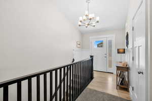 Corridor featuring light wood-style floors, a chandelier, lofted ceiling, an upstairs landing, and a wainscoted wall