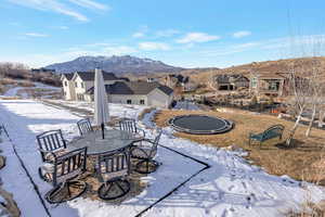 Snow covered patio featuring a trampoline, a mountain view, outdoor dining area, a residential view, and a patio area