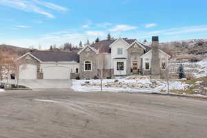French country home featuring stone siding, a garage, driveway, and a chimney