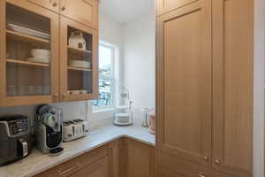 Bar area featuring glass insert cabinets, light stone countertops, and light brown cabinetry