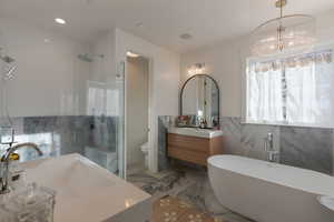 Full bathroom with a freestanding tub, vanity, tile walls, a stall shower, and light marble finish floors
