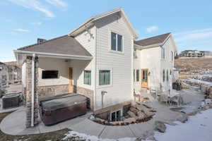 Snow covered house with a patio, a hot tub, outdoor dining area, roof with shingles, and stone siding