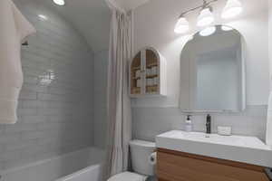 Full bath with shower / tub combo with curtain, vanity, tile walls, and tasteful backsplash