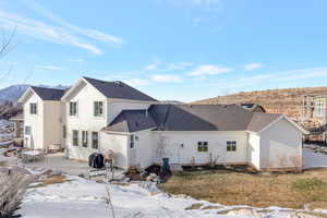 Snow covered house with a patio, a mountain view, and a shingled roof