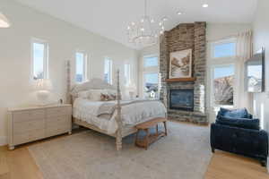 Bedroom with a stone fireplace, light wood-style flooring, a chandelier, and high vaulted ceiling