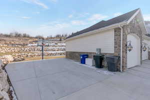 View of side of home with stone siding, a patio area, a garage, and a shingled roof