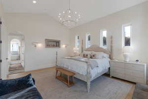 Bedroom with arched walkways, wood finished floors, multiple windows, a chandelier, and high vaulted ceiling