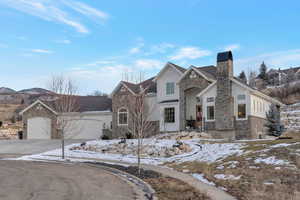 View of front of home with stone siding, a chimney, an attached garage, and driveway