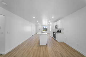 Kitchen with light countertops, a center island with sink, white cabinets, stainless steel appliances, and light wood finished floors