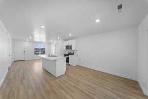 Kitchen with white cabinetry, a center island with sink, light countertops, stainless steel appliances, and light wood-style floors
