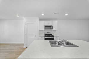 Kitchen with light countertops, stainless steel appliances, light wood-style flooring, white cabinets, and recessed lighting
