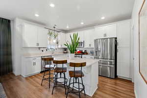 Kitchen featuring stainless steel appliances, a kitchen bar, white cabinets, decorative light fixtures, and recessed lighting