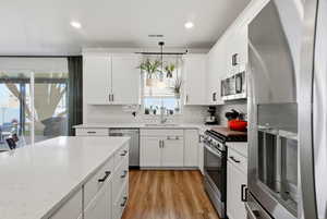 Kitchen featuring stainless steel appliances, white cabinetry, decorative light fixtures, light wood-type flooring, and recessed lighting