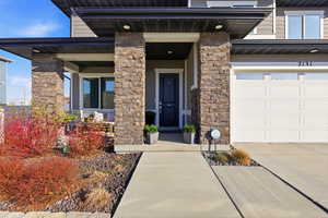 Doorway to property featuring stone siding, a garage, a porch, and driveway