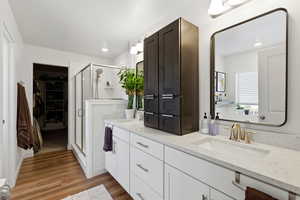Full bath featuring a spacious closet, double vanity, a shower stall, and light wood-style flooring