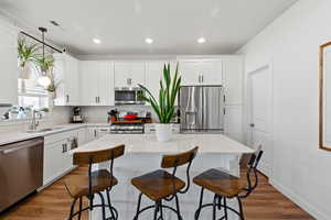 Kitchen with light stone countertops, white cabinetry, appliances with stainless steel finishes, and recessed lighting