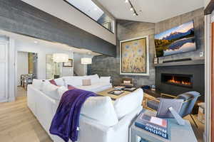 Living room with an accent wall, a glass covered fireplace, light wood-type flooring, and a high ceiling
