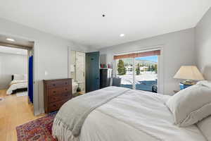 Bedroom with access to outside, light wood finished floors, ensuite bathroom, and recessed lighting
