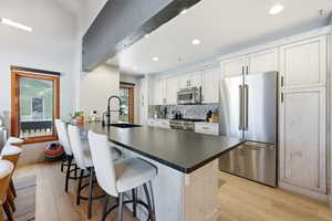 Kitchen featuring appliances with stainless steel finishes, a peninsula, light wood finished floors, a kitchen bar, and backsplash
