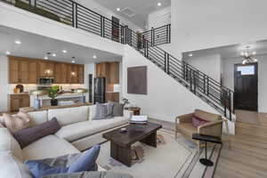 Living area featuring a high ceiling, light wood-style floors, recessed lighting, stairway, and a chandelier