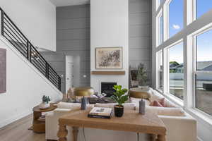 Living area featuring a towering ceiling, a glass covered fireplace, stairs, and wood finished floors