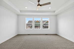 Empty room with a raised ceiling, light carpet, ceiling fan, and a textured ceiling